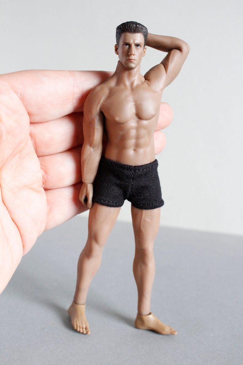 Puede incluir: Una figura de acci&oacute;n masculina musculosa con pantalones cortos negros. La figura tiene un f&iacute;sico esculpido y detallado y est&aacute; posada con un brazo levantado detr&aacute;s de la cabeza.