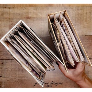 May include: Two open handmade photo albums with decorative pages. The albums have a white and gold color scheme. The pages are filled with various images and designs. The albums are displayed on a wooden surface.