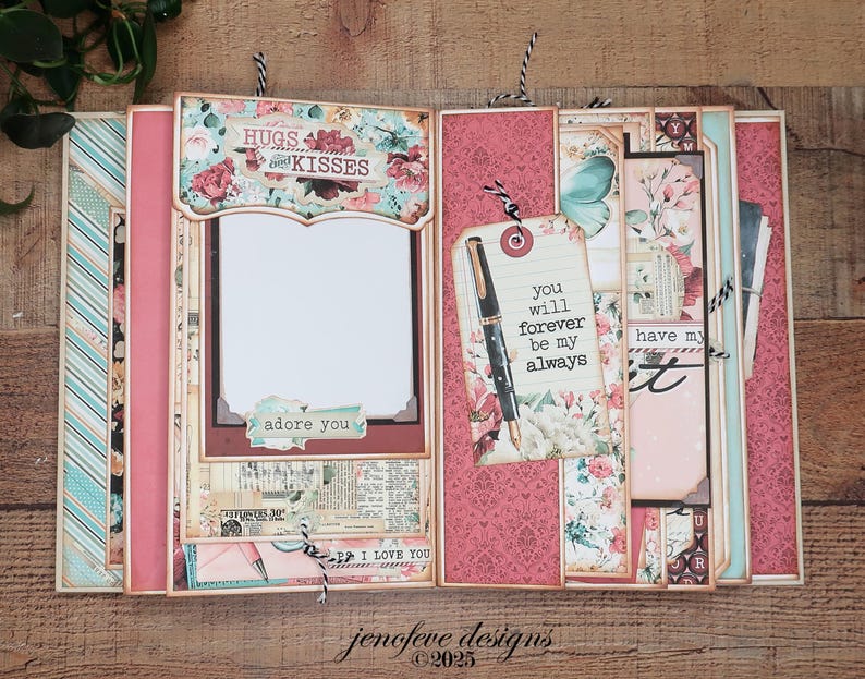 May include: A handmade scrapbook with a floral design, featuring pink, teal, and cream colors. The scrapbook includes decorative elements, tags with text, and a frame for a photo. The text includes "Hugs and Kisses", "adore you", and "I love you".