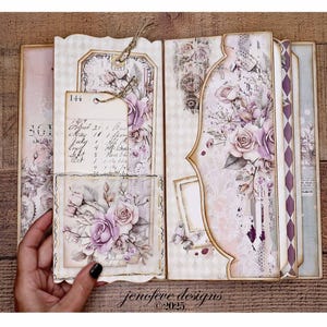 May include: Open scrapbook with floral and vintage-style designs. The pages feature soft pink and purple roses, decorative tags, and handwritten notes. The overall aesthetic is romantic and antique.