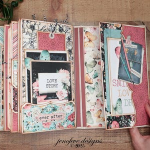 May include: Open scrapbook with floral and butterfly designs. The pages feature pink, blue, and cream colors with the words "Love Story" and "ever after." The scrapbook is open, revealing multiple pages and pockets.