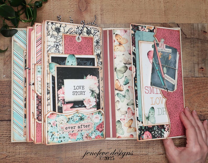 May include: Open scrapbook with floral and butterfly designs. The pages feature pink, blue, and cream colors with the words "Love Story" and "ever after." The scrapbook is open, revealing multiple pages and pockets.