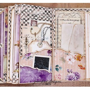 May include: A handmade scrapbook with a vintage aesthetic. The pages feature floral patterns, tags, and pockets. The color palette includes soft pinks, purples, and creams, with accents of black and white checkered patterns. The text "jenefere designs &copy;2025" is visible.