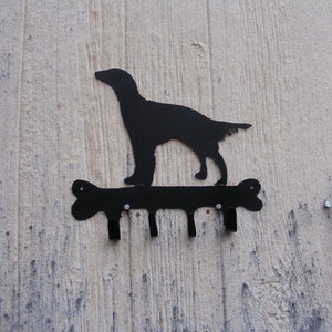 May include: Black metal key holder shaped like a dog standing on a bone. The key holder has four hooks.