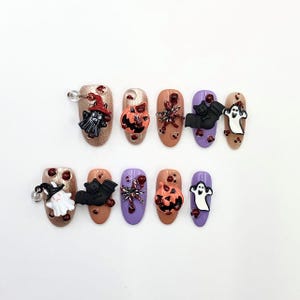 Può includere: Un set di dieci nail art a tema Halloween. Ogni unghia presenta un design diverso, tra cui un fantasma, un pipistrello, una zucca e un ragno. Le unghie sono dipinte in vari colori, tra cui oro, arancione, viola e marrone.