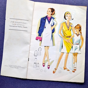 May include: Vintage fashion illustration featuring three figures in stylish dresses. The illustration includes the text "THE GOLDEN RULE. International Fashion Studio" and small sketches of clothing designs. The background is a blue surface.