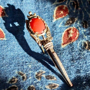 May include: A silver brooch with an ornate design and a large red gemstone in the centre.