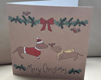 May include: A folded Christmas card with a brown background. The card features two dachshunds, one in a Santa suit and the other with a scarf, with a bird between them. The words "Merry Christmas" are written below.