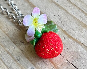 May include: A silver chain necklace with a red strawberry and a white flower charm. The strawberry is detailed with a green stem and leaves.