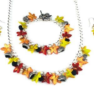 Puede incluir: Un conjunto de collar, pulsera y pendientes de cadena plateada con abalorios de hojas de oto&ntilde;o y bellotas. Los abalorios son en tonos rojos, naranjas, amarillos y verdes.