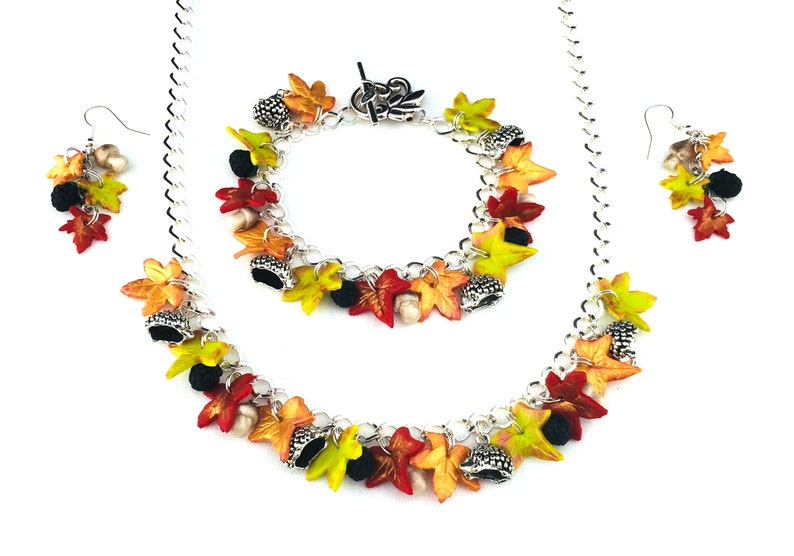 Puede incluir: Un conjunto de collar, pulsera y pendientes de cadena plateada con abalorios de hojas de oto&ntilde;o y bellotas. Los abalorios son en tonos rojos, naranjas, amarillos y verdes.
