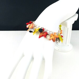 Puede incluir: Un brazalete de plata con dijes de tem&aacute;tica oto&ntilde;al. Los dijes est&aacute;n hechos de arcilla polim&eacute;rica y presentan hojas en tonos rojos, naranjas, amarillos y verdes. Tambi&eacute;n hay peque&ntilde;os dijes de bellota.