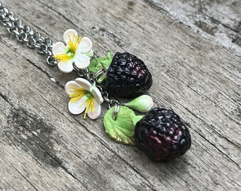 May include: A silver chain necklace with a charm featuring two blackberries and white flowers with yellow centers.
