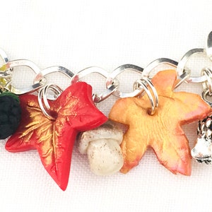 Puede incluir: Un brazalete de plata con dijes de tem&aacute;tica oto&ntilde;al, que incluyen una hoja roja, una hoja dorada, un hongo, una mora y un erizo.
