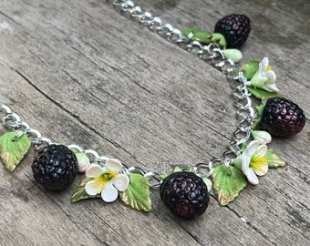 May include: A silver chain necklace with black and green polymer clay charms. The charms are shaped like blackberries and white flowers.