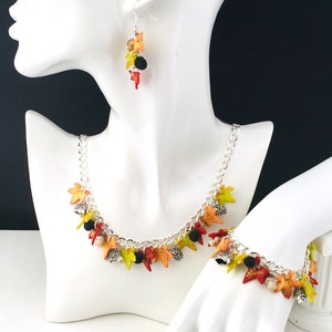 Puede incluir: Un collar y una pulsera de cadena plateada con dijes de tem&aacute;tica oto&ntilde;al. Los dijes est&aacute;n hechos de arcilla polim&eacute;rica y presentan hojas en tonos naranja, amarillo y verde, as&iacute; como peque&ntilde;as cuentas negras.
