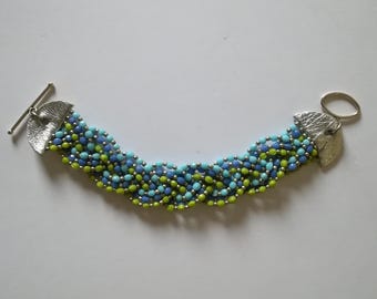 Gevlochten armband met meerdere strengen, gemaakt van glaskralen en leer, handgemaakt, origineel ontwerp, met knevelsluiting.