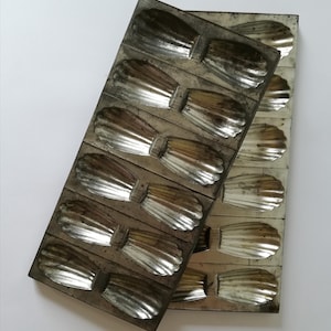 Op de afbeelding: Twee vintage metalen bakvormen met een gegolfd ontwerp. De vormen zijn gemaakt van zilverkleurig metaal en hebben een versleten, antieke uitstraling.