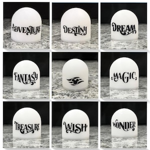 May include: White, dome-shaped decorative objects with black text. The text includes words like "Adventure," "Destiny," "Dream," "Fantasy," "Magic," "Treasure," "Wish," and "Wonder." One object features a black Mickey Mouse head logo.