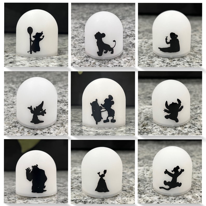 May include: Nine white dome-shaped night lights with black silhouette images of Disney characters. The characters include Mickey Mouse, Stitch, Simba, and more.