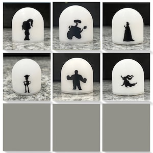 May include: Set of six white dome-shaped night lights with black silhouettes of Disney characters. The characters include: Woody, Buzz Lightyear, Sulley, Mike Wazowski,  Boo, and Ursula.