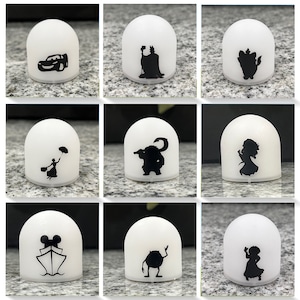May include: Nine white dome-shaped night lights with different Disney character silhouettes. The characters include:  Cars,  Maleficent,  Ariel,  The  Beast,  Mary Poppins,  Sulley,  Mickey Mouse,  Mike Wazowski, and  Tiana.