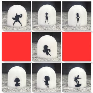 May include: White, dome-shaped night lights featuring black silhouettes of animated characters. The collection includes various poses, such as a superhero stance, a standing figure, and a surfing pose. The lights are arranged in a grid pattern.