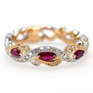 May include: A delicate gold and white band ring with three marquise-shaped ruby gemstones set in a twisted design. The ring is adorned with small diamonds.
