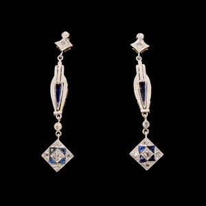 May include: A pair of silver dangle earrings with blue and white gemstones. The earrings feature a geometric design with a square-shaped pendant.
