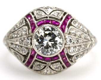 Puede incluir: Un anillo de platino vintage con un gran diamante redondo brillante en el centro rodeado por un halo de diamantes más pequeños y una banda de acentos de rubí.