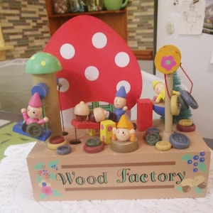 May include: A wooden toy music box with a red and white mushroom, colorful gnomes, and a sign that reads "Wood Factory".