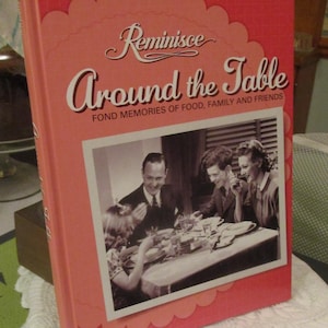 May include: A hardcover book titled "Reminisce Around the Table" with a pink cover and a black and white photo of people dining. The book's cover has the text "Fond Memories of Food, Family and Friends".