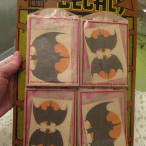 May include: Vintage IMPKO decals featuring bat designs in black and orange. The decals are packaged in individual cellophane packets, arranged on a cardboard backing. The packaging includes the text "DECALS" and "Don't forget SOUVENIRS for your friends."