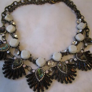 May include: A two-strand necklace with a gold chain and white, iridescent, and black beads. The necklace features a layered design with a cluster of black and white beads at the center.