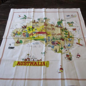 May include: White rectangular tea towel featuring a colorful map of Australia with cartoon illustrations of landmarks and animals. The word "AUSTRALIA" is printed in a yellow banner. The towel has a brown border.