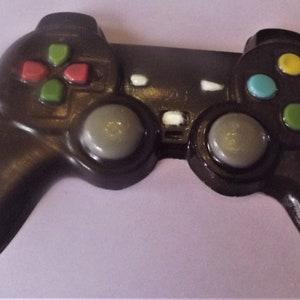 May include: A dark brown video game controller with colorful buttons. The controller has a directional pad with red and green buttons, and four colored buttons: yellow, blue, red, and green. Two gray joysticks are also visible.