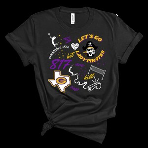 Puede incluir: Camiseta negra con un diseño de voleibol. El diseño incluye el texto "Let's Go Lady Pirates", "dig, hit, ace, kill, set" y "established 1866". También aparece un logotipo con la forma de Texas.