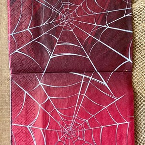Puede incluir: Dos servilletas de papel rojas con un dise&ntilde;o de telara&ntilde;a blanca. El dise&ntilde;o de la telara&ntilde;a es un patr&oacute;n radial con el centro de la telara&ntilde;a en la parte inferior de la servilleta.