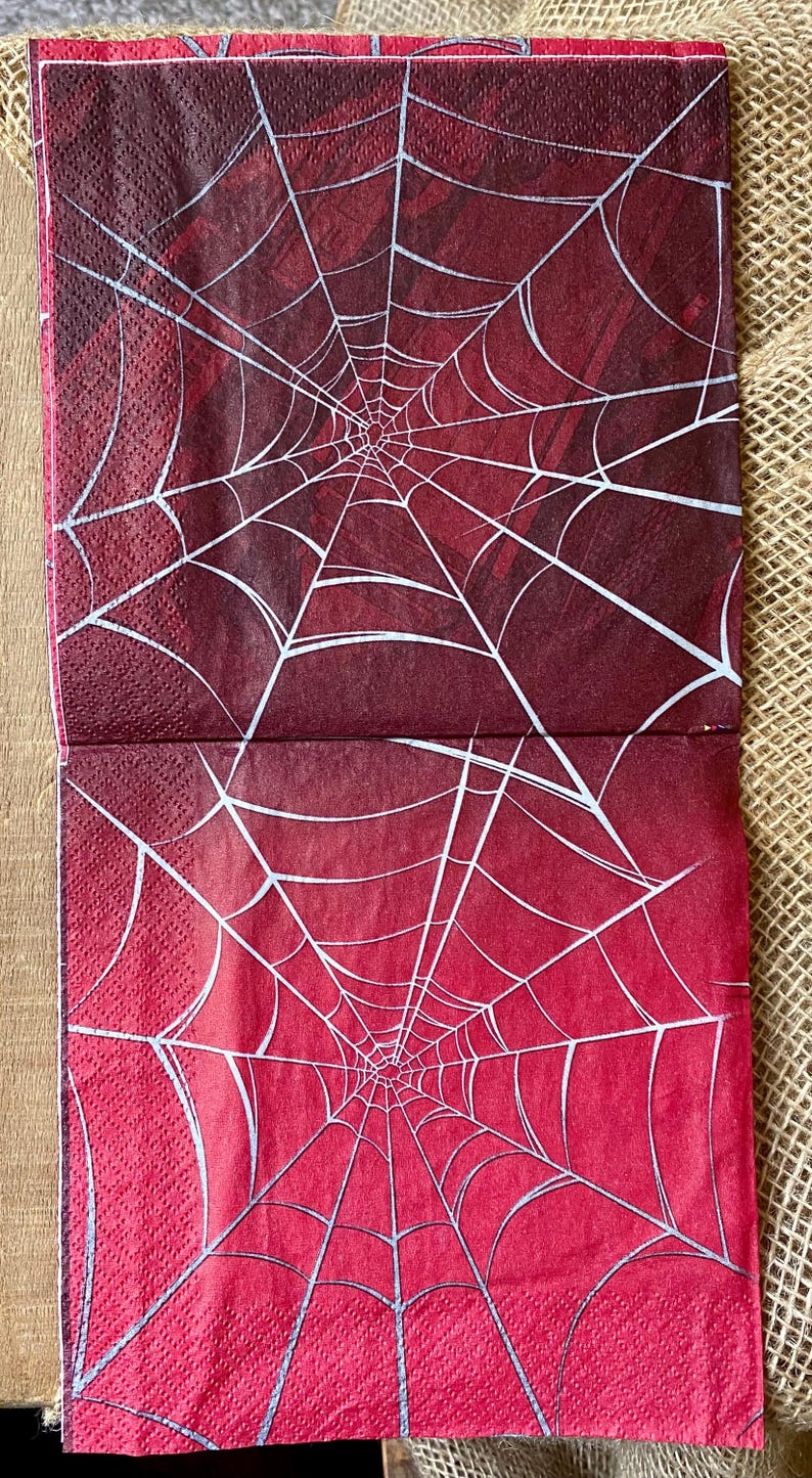 Puede incluir: Dos servilletas de papel rojas con un dise&ntilde;o de telara&ntilde;a blanca. El dise&ntilde;o de la telara&ntilde;a es un patr&oacute;n radial con el centro de la telara&ntilde;a en la parte inferior de la servilleta.