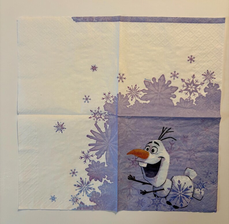 May include: A square paper napkin featuring a light purple and white color scheme with a pattern of various snowflakes. The character Olaf is printed in the bottom right corner, depicted with a carrot nose, wide smile, and stick-like arms.