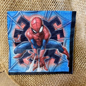 May include: A square paper napkin featuring a graphic illustration of the superhero Spider-Man in a crouching pose. The character is red and blue with a black web pattern, set against a blue background with a dark spider web design.