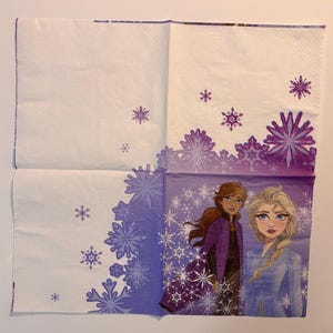 May include: A square paper napkin featuring a white background with purple snowflake patterns. The bottom right quadrant displays an illustration of two characters, one with long brown hair in a purple jacket and one with blonde hair in a blue outfit.