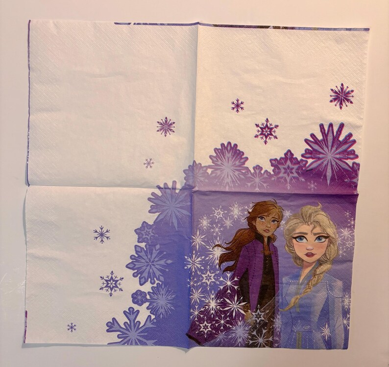 May include: A square paper napkin featuring a white background with purple snowflake patterns. The bottom right quadrant displays an illustration of two characters, one with long brown hair in a purple jacket and one with blonde hair in a blue outfit.