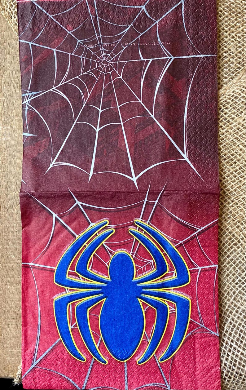Puede incluir: Servilleta de papel roja y blanca con un dise&ntilde;o de telara&ntilde;a azul y amarilla. La telara&ntilde;a tiene la forma de una ara&ntilde;a. El texto "MARVEL" est&aacute; impreso en la servilleta.
