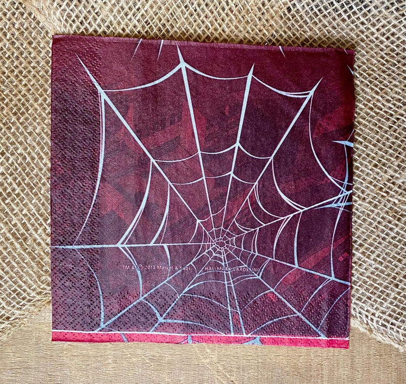 Puede incluir: Servilleta de papel roja con un dise&ntilde;o de telara&ntilde;a blanca. El texto "Hallmark Cards Inc." est&aacute; impreso en la servilleta.