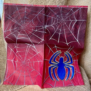 Puede incluir: Servilletas de papel rojas y blancas con un dise&ntilde;o de telara&ntilde;a. Una servilleta presenta una ara&ntilde;a azul con un contorno amarillo.