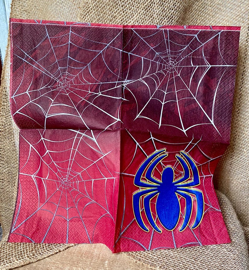 Puede incluir: Servilletas de papel rojas y blancas con un dise&ntilde;o de telara&ntilde;a. Una servilleta presenta una ara&ntilde;a azul con un contorno amarillo.