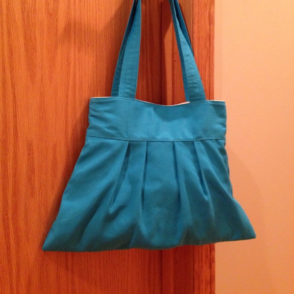 Blue handbag, pleated, canvas lined, over the shoulder, snap closure.