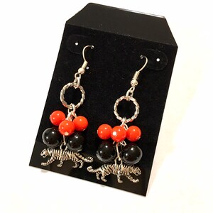 May include: A pair of dangle earrings with black and red beads and silver tiger charms.