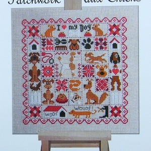 Puede incluir: Un bordado de punto de cruz sobre una tela beige con un marco de madera. El diseño presenta un patchwork de varias razas de perros, incluyendo un caniche, un dachshund, un bulldog y un terrier. El texto "Amo a mi perro" está bordado en el centro del diseño. Las palabras "woof" y "wouaf!" también están bordadas en el diseño.